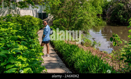 Asian woman with blue veste, jupe et chaussures de marche et le port de lunettes de soleil chemin descendant à côté de canal Banque D'Images