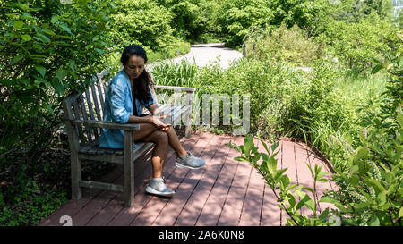 Asian woman sitting on bench in botanical gardens Banque D'Images