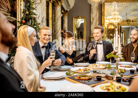 Élégamment vêtue groupe de personnes ayant un dîner de fête à une table bien servie, la célébration de nouvelle année de vacances au restaurant de luxe Banque D'Images