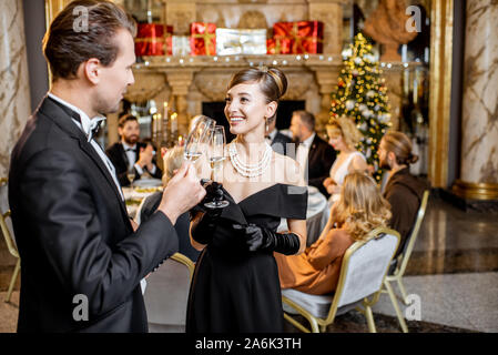 Belle bien habillés couples célébrant le Nouvel An, se tenant ensemble avec sparcle vin au restaurant de luxe avec d'autres personnes sur l'arrière-plan Banque D'Images