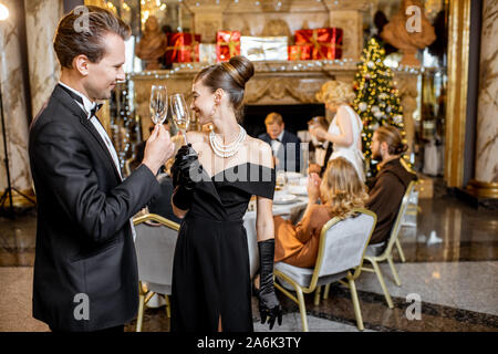 Belle bien habillés couples célébrant le Nouvel An, se tenant ensemble avec sparcle vin au restaurant de luxe avec d'autres personnes sur l'arrière-plan Banque D'Images