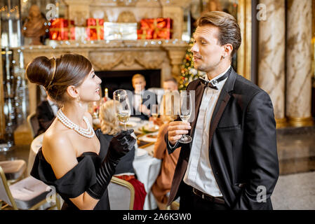 Belle bien habillés couples célébrant le Nouvel An, se tenant ensemble avec sparcle vin au restaurant de luxe avec d'autres personnes sur l'arrière-plan Banque D'Images