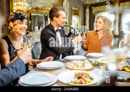 Élégamment vêtue groupe de personnes ayant un dîner de fête à une table bien servie, la célébration de nouvelle année de vacances au restaurant de luxe Banque D'Images