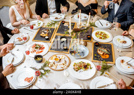 Les personnes ayant un dîner de fête à une table bien servie avec de savoureux plats internationaux au cours de l'Année restaurant de luxe Banque D'Images