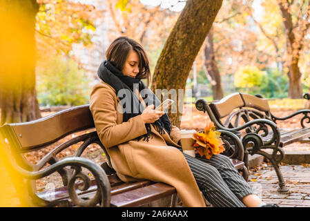 Femme assise au parc de la ville de boire du café de prendre photo de bouquet de feuilles d'érable Banque D'Images