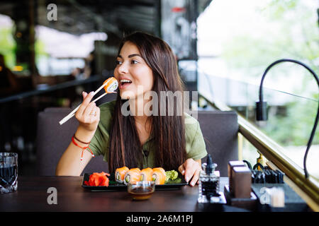 Young Woman eating sushi frais et profiter en restaurant de luxe. Female client holding bâtonnets et de manger des repas orientaux sur le déjeuner. Banque D'Images