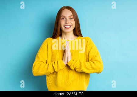 Cheerful young redhead rousseur femme faisant prier geste, gardant paumes ensemble, souriant largement, demande à mari pour acheter son nouveau sac à main isol Banque D'Images