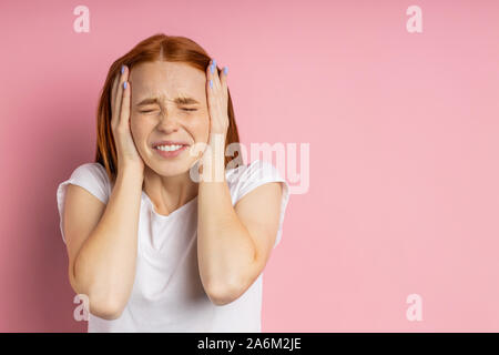 Closeup portrait de jeune femme rousse stressantes de rousseur couvrant les oreilles avec des palmiers et de fermeture yeux serrés,agacé par le bruit fort, avoir des maux de tête, m Banque D'Images