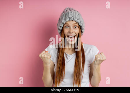 Rousseur redhead Caucasian woman in Casual t-shirt, chapeau tricoté réjouissance sa victoire et le succès, work, criant de bonheur plus retour rose Banque D'Images