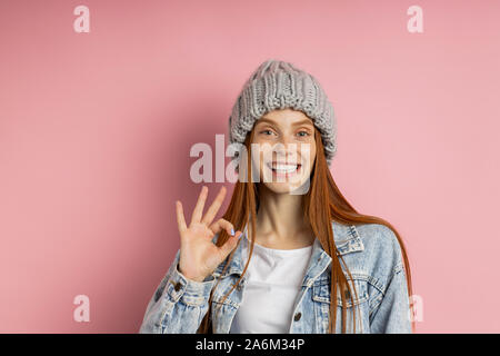 Cheerful redhead femme vêtue de viper, encombrantes étoffes hat faire bon geste, démontrer, accord parfait avec sourire dents blanches isola Banque D'Images