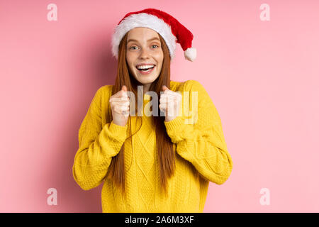 Coup de jeune rouquine joyeuse happy girl with long hair wearing Santa hat work, encourager quelqu'un ou se réjouir, souriant à la victoire à c Banque D'Images