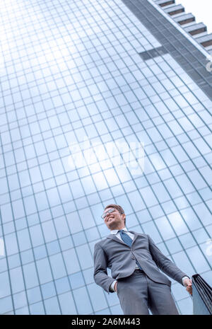 Business man with briefcase debout sur l'herbe près de tall office building Banque D'Images