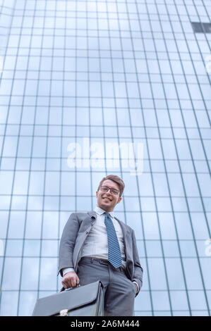 Business man with briefcase debout sur l'herbe près de tall office building Banque D'Images