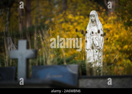 Avis de cimetière lituanienne en automne. Sculpture en pierre blanche de deuil - Marie et Pierre tombale croix entre fleurs et arbres à fleurs jaunes Banque D'Images