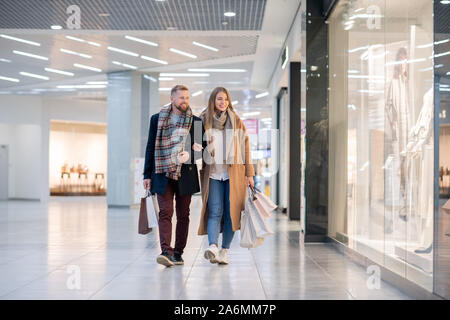 Young affectionate couple dans casualwear se déplaçant le long des vitrines dans le centre commercial Banque D'Images