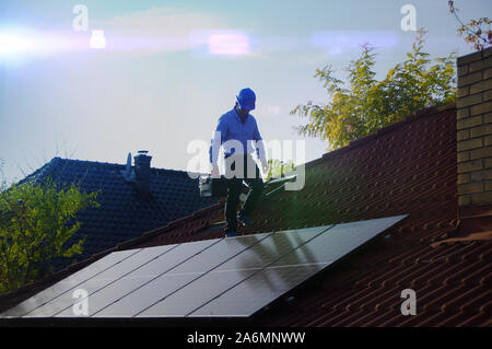 L'homme marche sur toit de maison et installe des panneaux solaires. L'énergie photovoltaïque, l'énergie alternatives et renouvelables, l'énergie verte, l'écologie et la production d'électricité Banque D'Images