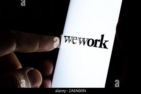 WeWork logo de l'entreprise sur l'écran du smartphone dans une pièce sombre et un doigt pointant sur elle. WeWork fournit l'espace de bureau et l'espace de solutions. Banque D'Images