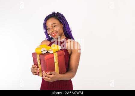 Une fille à la peau sombre est titulaire d'un énorme cadeau rouge avec un arc d'or dans ses mains, regarde la caméra et sourit. Concept de maison de vacances, Nouvel an et de noël, re Banque D'Images