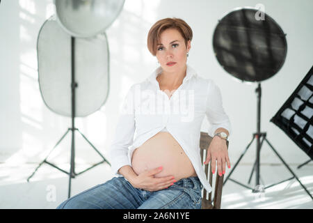 Femme enceinte d'âge moyen est assis sur une chaise au milieu d'un Studio Photo Banque D'Images