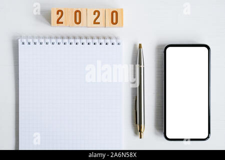 Maquette du smartphone, feuille de carnet à spirales, métal stylo en bois, cubes à l'année 2020 nouveaux numéros symbolisant sur fond blanc. Banque D'Images