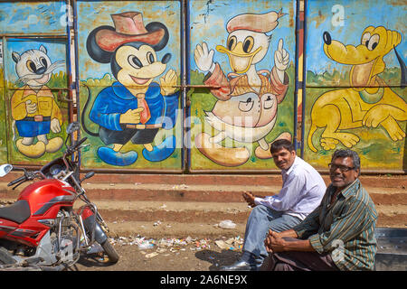 Dans une zone à l'abandon de Mumbai, Inde, deux hommes assis devant une peinture murale représentant Mickey Mouse, Donald Duck et des autres personnages de Disney Banque D'Images