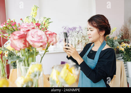 Fleuriste jeune Vietnamien qui pose photos de bouquets finis sur les médias sociaux Banque D'Images
