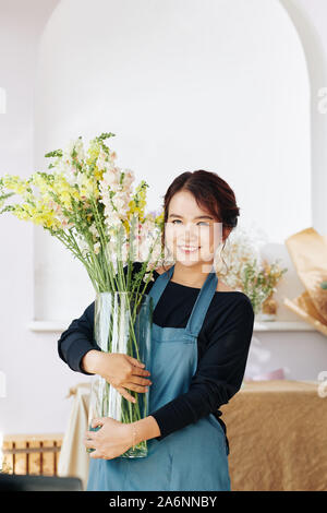 Portrait de jeune femme heureuse en tablier bleu holding big glass Vase avec fleurs Banque D'Images