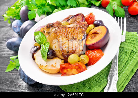 Poulet cuit au four avec tomates, pommes, prunes et raisins dans un plat sur une serviette, ail, persil et basilic sur planche de bois contexte Banque D'Images