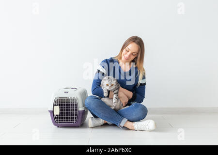 Charmante jeune femme positive tient dans ses mains son beau chat Scottish Fold gris assis sur le plancher d'un nouvel appartement. Concept d'animaux. Banque D'Images