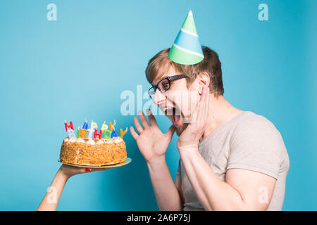 Fou drôle jeune homme dans un papier de souhaits hat veut mordre dans un morceau de gâteau de félicitations. Concept de fricoter et voeux d'anniversaire. Copie Banque D'Images