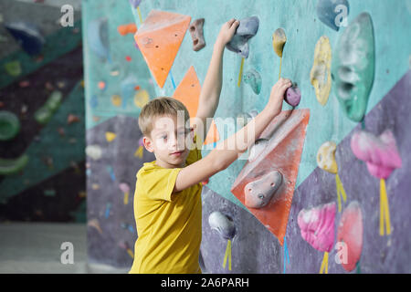 Écolier active t-shirt jaune à l'accaparement de terres par les roches artificielles sur mur d'escalade Banque D'Images