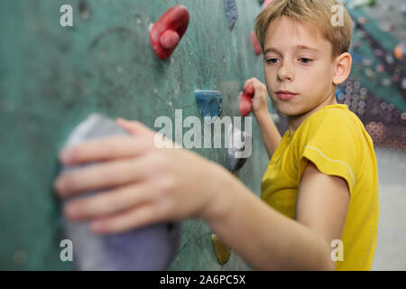 Jeune écolier en jaune t-shirt tenue par de petites roches sur mur d'escalade Banque D'Images