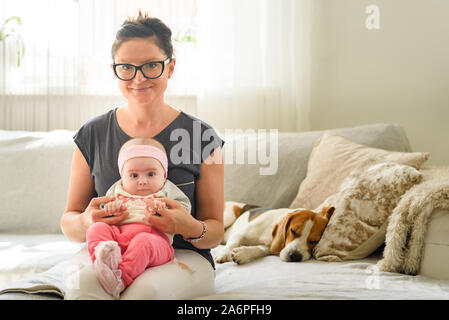 Mother holding magnifique petite fille en lumineuse, ensoleillée. Chien Beagle reposant sur la table en arrière-plan la maternité concept Banque D'Images