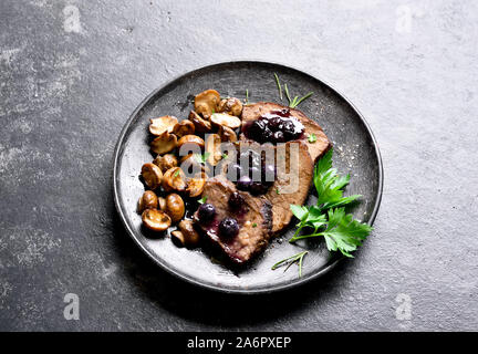 Boeuf mijotés avec champignons et sauce aux bleuets sur pierre sombre arrière-plan. La viande en ragoût savoureux avec champignons et sauce douce. Vue rapprochée Banque D'Images