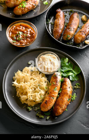 Saucisses grillées avec de la choucroute et au raifort sur plaque sur fond noir en noir Banque D'Images