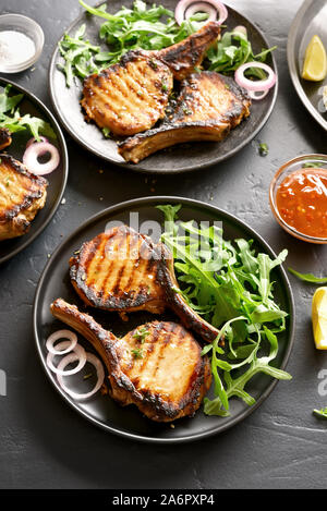 Steaks de porc grillé avec des greens sur plaque sur fond noir en noir. Banque D'Images