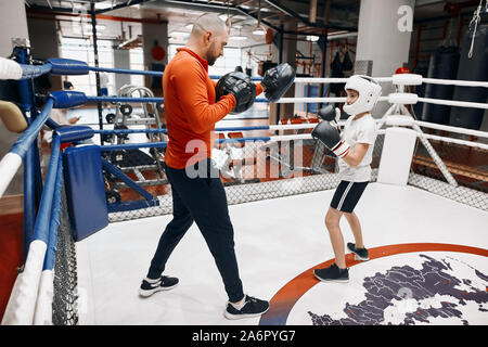 Petit garçon joyeux combat avec son formateur, pleine longueur latérale sur la photo. Banque D'Images