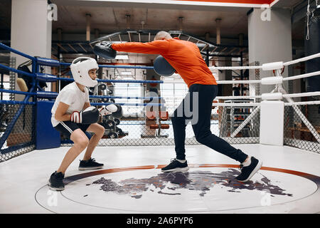 Peu de formation et de faire l'entraînement de boxeur avec jeune homme . Les techniques de combat, pleine longueur photo. Vue de côté . Banque D'Images