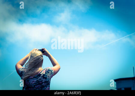 Dame caucasienne blonde avec des sacs bandoulière photo prise d'un téléphone cellulaire contre le ciel bleu Banque D'Images