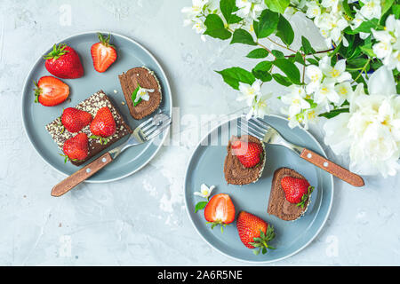 Rollcake chocolat avec fraises fraîches sur plaque en céramique, de jasmin et de pivoines blanches sur la surface de béton gris clair table. Haut de la vue, télévision lay, copie Banque D'Images