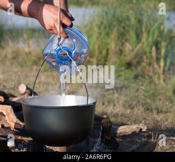 L'ajout d'eau à partir de la grosse bouteille en plastique en noir utilisé chaudron sur feu ouvert, repas camping Banque D'Images