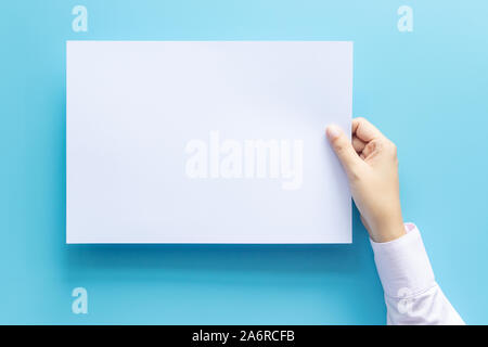 Close up hands holding empty white blank lettre format de papier A4 pour flyer ou invitation maquette isolé sur un fond bleu. Banque D'Images