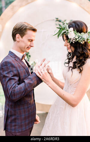 Couple de mariage anneaux change lors de la cérémonie du mariage en plein air. Mariée avec un bouquet de fleurs et de verdure et le marié en costume élégant avec arch sur Banque D'Images