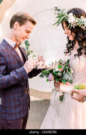 Couple de mariage anneaux change lors de la cérémonie du mariage en plein air. Mariée avec un bouquet de fleurs et de verdure et le marié en costume élégant avec arch sur Banque D'Images