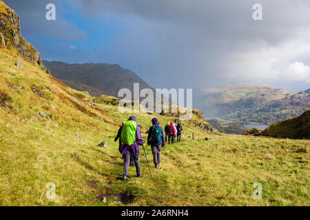Groupe de Randonneurs marchant dans le soleil et la pluie au-dessus de Nant Gwynant dans les collines du Parc National de Snowdonia. , Beddgelert Gwynedd, au nord du Pays de Galles, Royaume-Uni, Angleterre Banque D'Images
