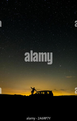 Voie lactée photo sur une nuit d'été. Un ciel plein d'étoiles.Un homme contre la lumière entre dans sa voiture pour essayer d'attraper une étoile. Banque D'Images