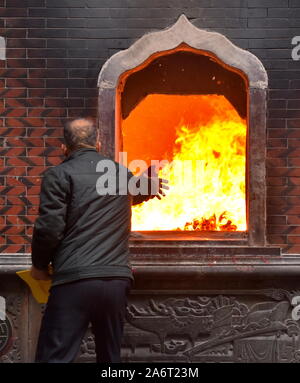 Man joss lance les offres de papier à brûler dans le feu de l'Tonghuai temple Guanyue de religion à Quanzhou Banque D'Images