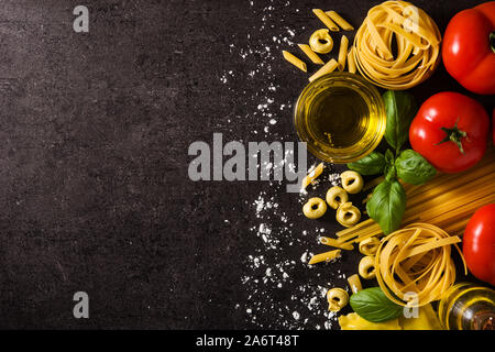 Les pâtes italiennes et les ingrédients. Ravioli, pâtes penne, spaghetti, tortellini, tomates et basilic sur fond noir. Top View copy space Banque D'Images