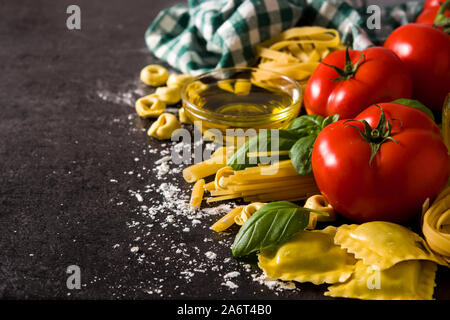 Les pâtes italiennes et les ingrédients. Ravioli, pâtes penne, spaghetti, tortellini, tomates et basilic sur fond noir. Copy space Banque D'Images