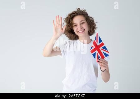 Bonjour ! Belle jeune femme aux cheveux bouclés avec une grande bretagne drapeau sur un fond clair. Apprendre l'anglais. Banque D'Images